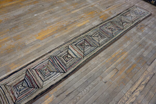 Textured runner featuring multicolored concentric diamond patterns rests on distressed gray wooden floorboards.