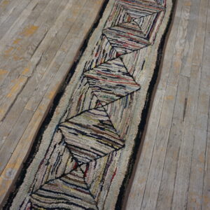 A textured, multi-colored runner rug with a repeating diamond pattern rests on distressed gray wood planks.