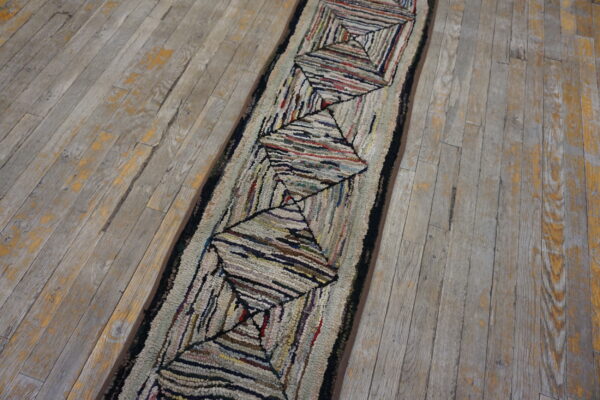 A textured, multi-colored runner rug with a repeating diamond pattern rests on distressed gray wood planks.