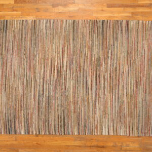 Textural rug with thin, vertical stripes in varied earth tones rests on warm hardwood flooring.
