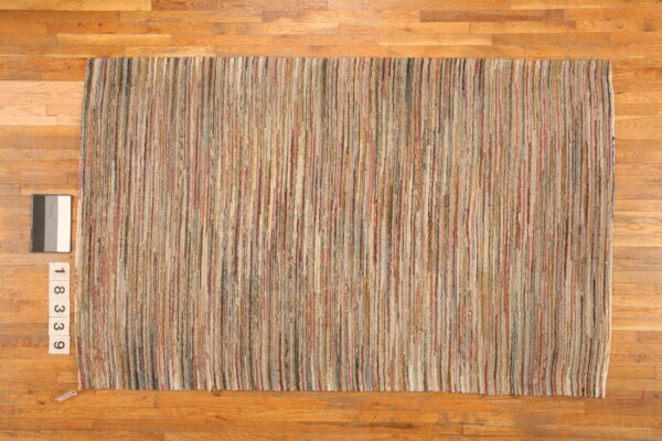 Textural rug with thin, vertical stripes in varied earth tones rests on warm hardwood flooring.