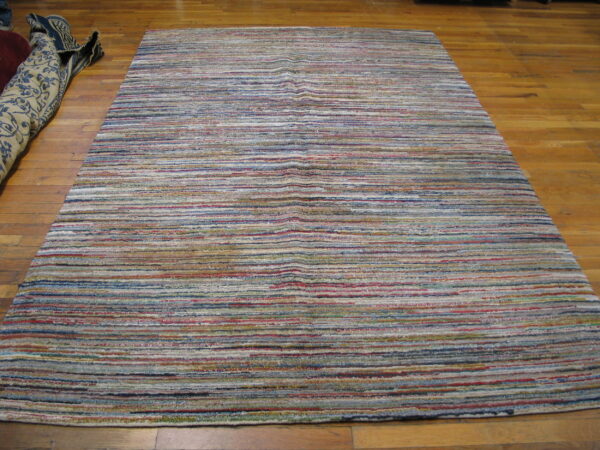 Textured multicolor striped rug featuring horizontal bands of blue, red, cream, and gray on wood planks.