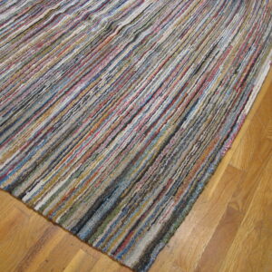 High-texture multicolored strip rug in blues, reds, grays, and yellows, angled over golden hardwood planks.