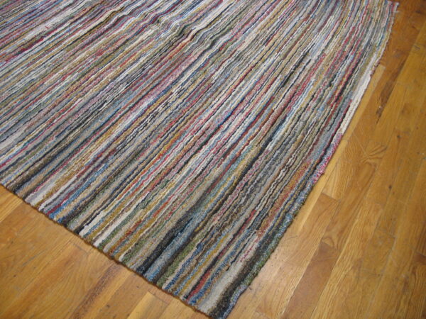High-texture multicolored strip rug in blues, reds, grays, and yellows, angled over golden hardwood planks.