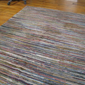Textured rug with varied horizontal multicolor stripes sits on a polished hardwood floor.