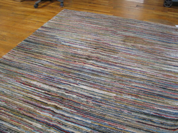 Textured rug with varied horizontal multicolor stripes sits on a polished hardwood floor.