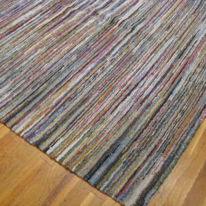 Multicolored textured rug featuring thick, variegated stripes lays diagonally on light wood floorboards.