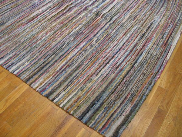 Multicolored textured rug featuring thick, variegated stripes lays diagonally on light wood floorboards.
