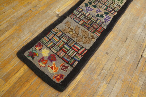 Hooked runner rug with alternating multicolored striped blocks and botanical designs, set on distressed wood flooring.