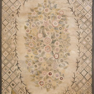 Low pile rug in beige with a central pastel floral design bordered by a diamond lattice pattern.