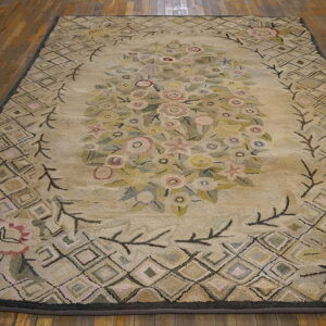 Beige rug with a central floral design and diamond trellis border resting on rustic wood floor.