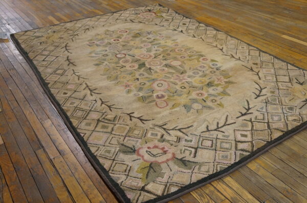 Textured floral rug in beige, pink, and green colors featuring a lattice border, laid on rustic wood planks.