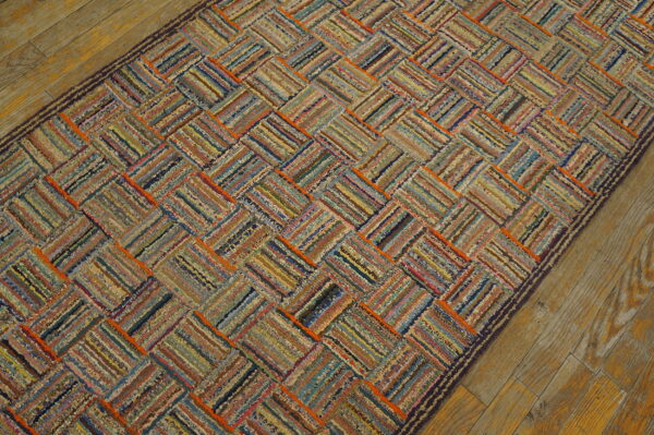 A multicolored textured rag rug runner features a diagonal basketweave pattern on rustic wood floor.