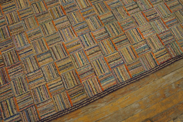 Textured rag rug in faded blues, browns, and oranges, displaying a woven block pattern on wood flooring.