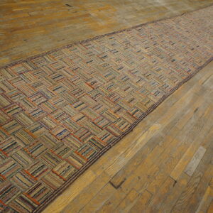 Textured runner rug with a striped, multicolored herringbone pattern on wide plank hardwood flooring.