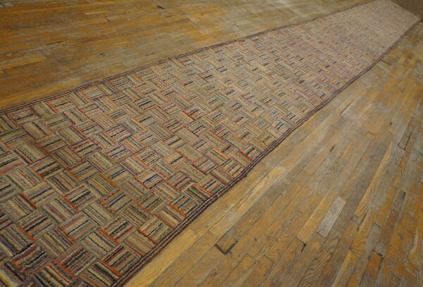 Textured runner rug with a striped, multicolored herringbone pattern on wide plank hardwood flooring.