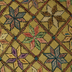 Textured olive green rug with multicolored star motifs in a diagonal grid, bordered by blue and wood floor.