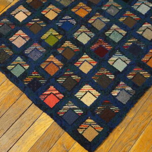Textured navy blue rug with a multicolored patchwork diamond design on golden wood planks.