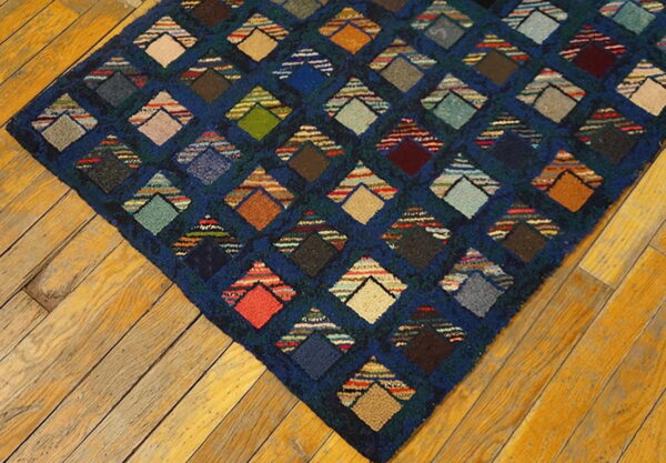 Textured navy blue rug with a multicolored patchwork diamond design on golden wood planks.