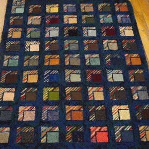 A deep blue rug with a grid of multicolored patchwork squares covers light wood plank flooring.