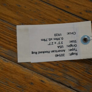 A paper inventory tag secured with wire rests diagonally across worn, brown hardwood planks.
