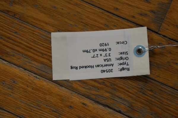 A paper inventory tag secured with wire rests diagonally across worn, brown hardwood planks.