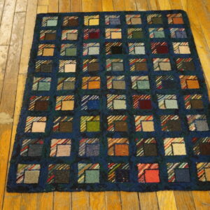 Dark blue rug with high pile features multicolor squares resembling a patchwork quilt on worn wood planks.