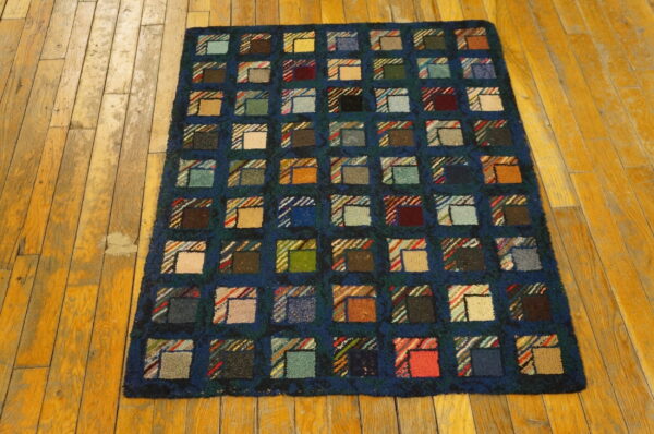 Dark blue rug with high pile features multicolor squares resembling a patchwork quilt on worn wood planks.