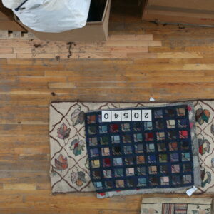 Patchwork blue and multicolored square rug covers a partial tan rug with a vine and leaf motif.