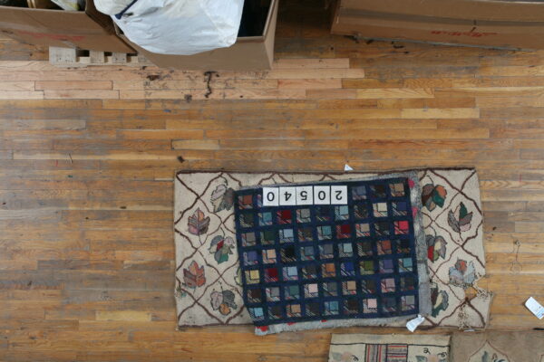 Patchwork blue and multicolored square rug covers a partial tan rug with a vine and leaf motif.
