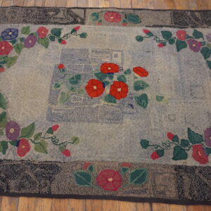 Textured rug featuring red, blue, and purple floral vines and a dark border, set on wood flooring.