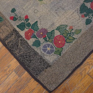 Gray and floral looped rug corner with a speckled border rests on distressed light brown wood flooring.
