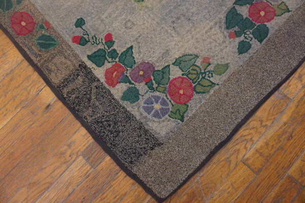 Gray and floral looped rug corner with a speckled border rests on distressed light brown wood flooring.