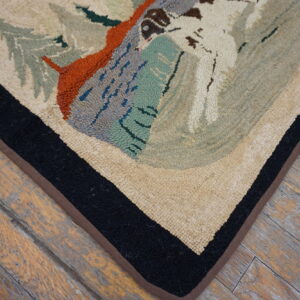 Pictorial hooked rug in cream, slate, and orange with a bold black border lies on distressed wood floors.