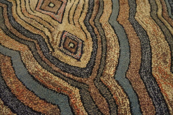 High-texture rug featuring concentric wavy bands and diamond motifs in brown, beige, blue, and black loops.
