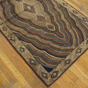 Textured rug with wavy concentric bands in tan, brown, teal, and blue on wood flooring.