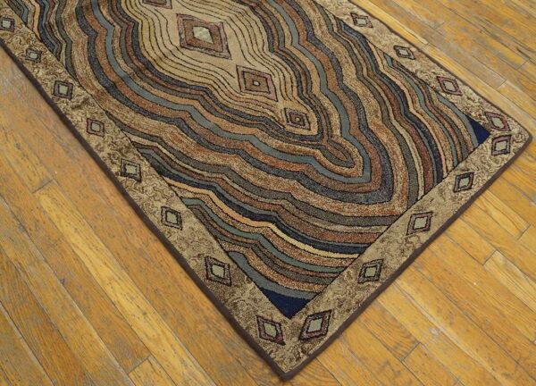 Textured rug with wavy concentric bands in tan, brown, teal, and blue on wood flooring.