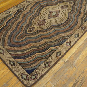 Textured, multicolor rug displaying wavy brown, beige, blue, and green bands with geometric border elements on hardwood.