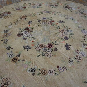 Beige round rug with floral and bird patterns in muted purple, brown, and pink on wood floor.