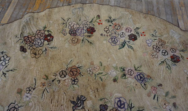 Round, textured beige rug with a dense pattern of multi-colored florals rests on weathered wood planks.