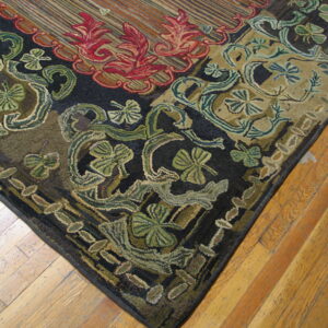 Textured corner of a dark rug featuring large red and green botanical motifs on natural hardwood flooring.