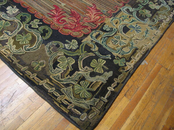 Textured corner of a dark rug featuring large red and green botanical motifs on natural hardwood flooring.