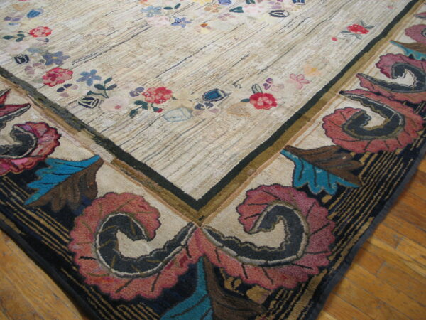 Textured rug corner showing a light field with small flowers and a deep border of stylized teal and rose foliage.