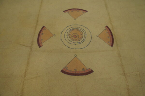 Tan, low-pile rug featuring a geometric cross pattern of numbered orange quadrants and blue concentric target rings.