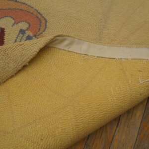 A light yellow looped-pile rug, partially rolled, shows abstract pink and blue shapes on rustic wood floors.