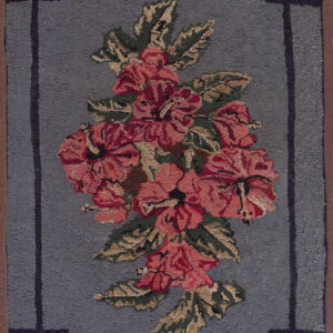 A dusty blue textured rug features a large pink and red floral cluster and a geometric inner border.