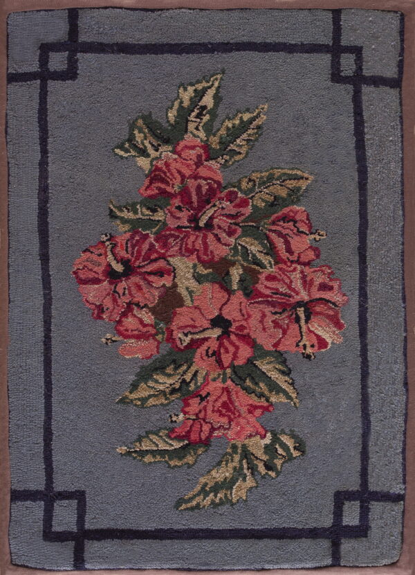 A dusty blue textured rug features a large pink and red floral cluster and a geometric inner border.