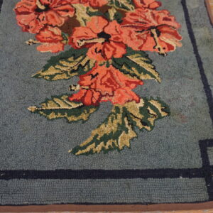 Loop pile rug in dusty blue with coral floral pattern and dark border on weathered wood planks.