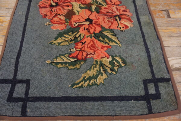 Loop pile rug in dusty blue with coral floral pattern and dark border on weathered wood planks.