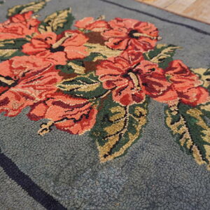 Nubby blue-gray rug featuring large coral and green floral motifs, shown close-up on a wood floor.
